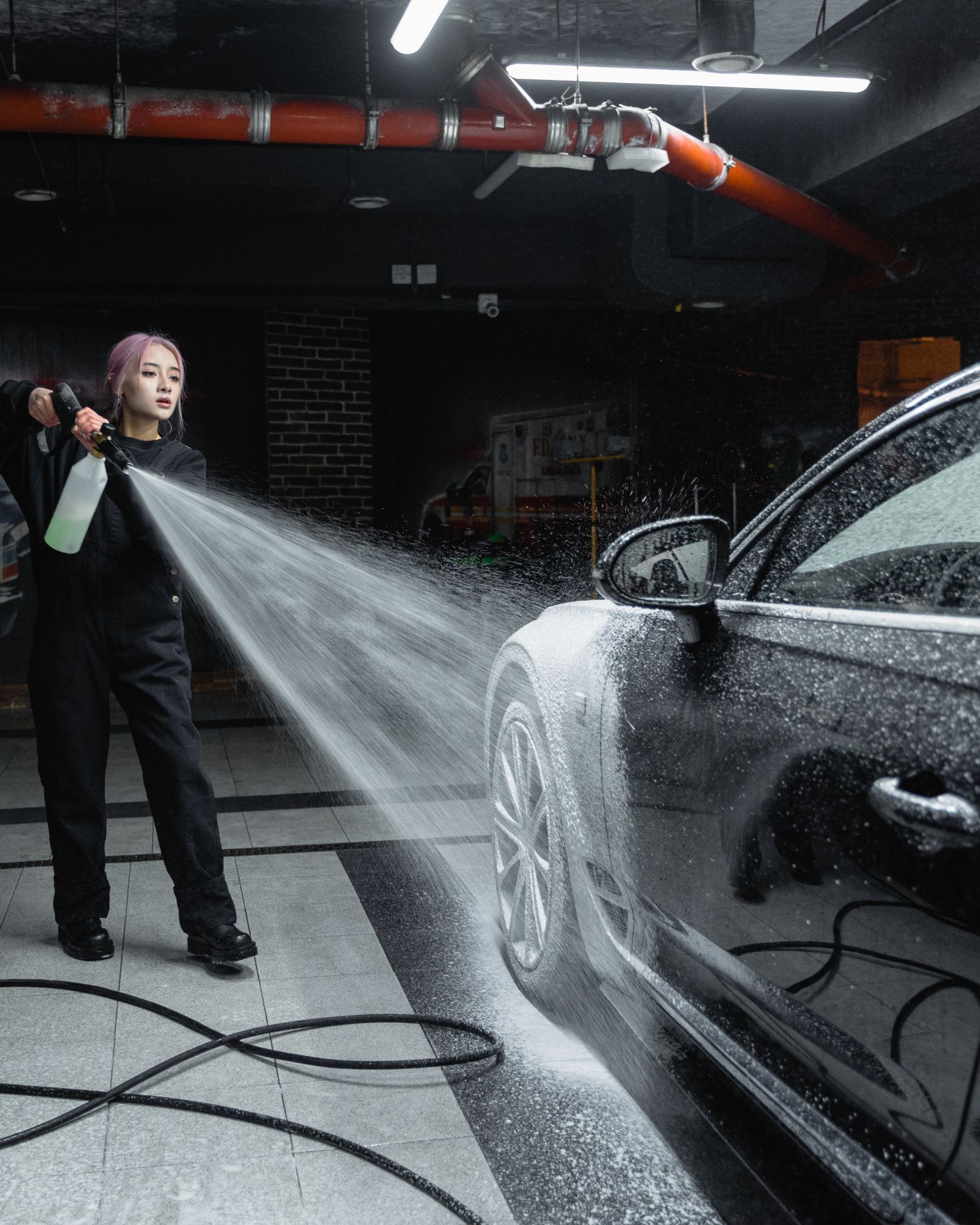 A man with tattoos is washing a car in a garage.
