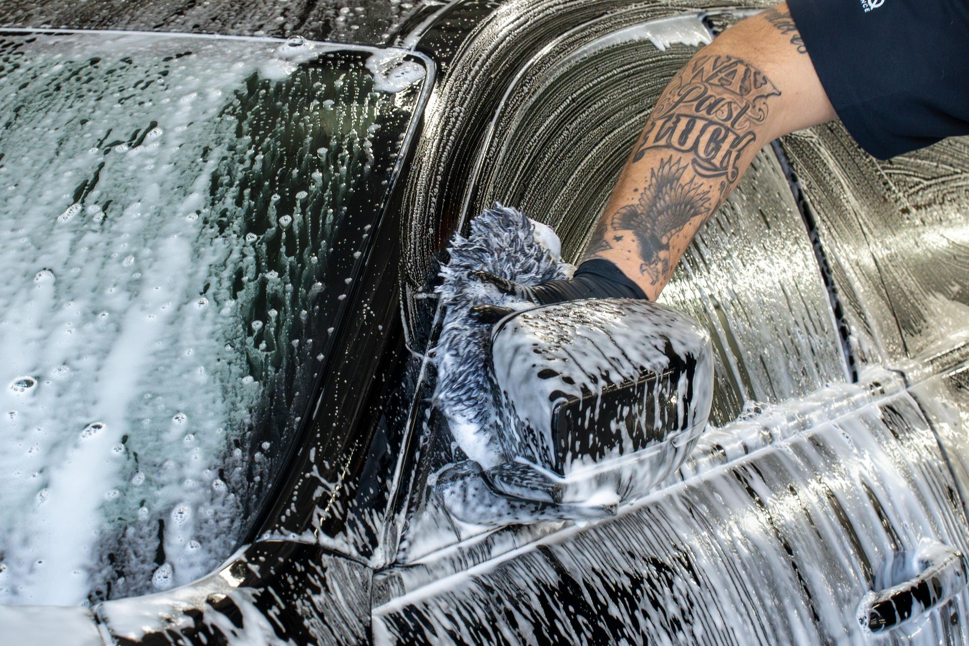 A person with a tattoo on their arm is washing a car.