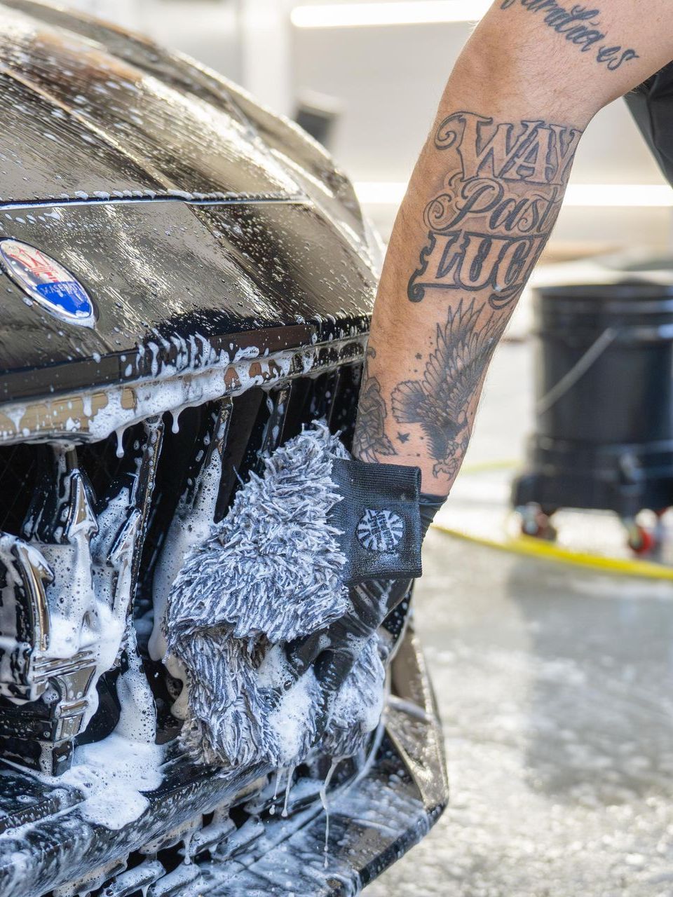 A man with a tattoo on his arm is washing a car.