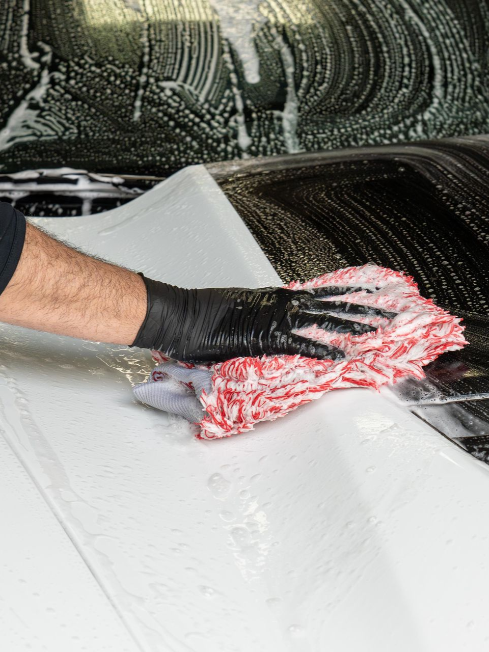 A person is washing a white car with a yellow spray bottle.