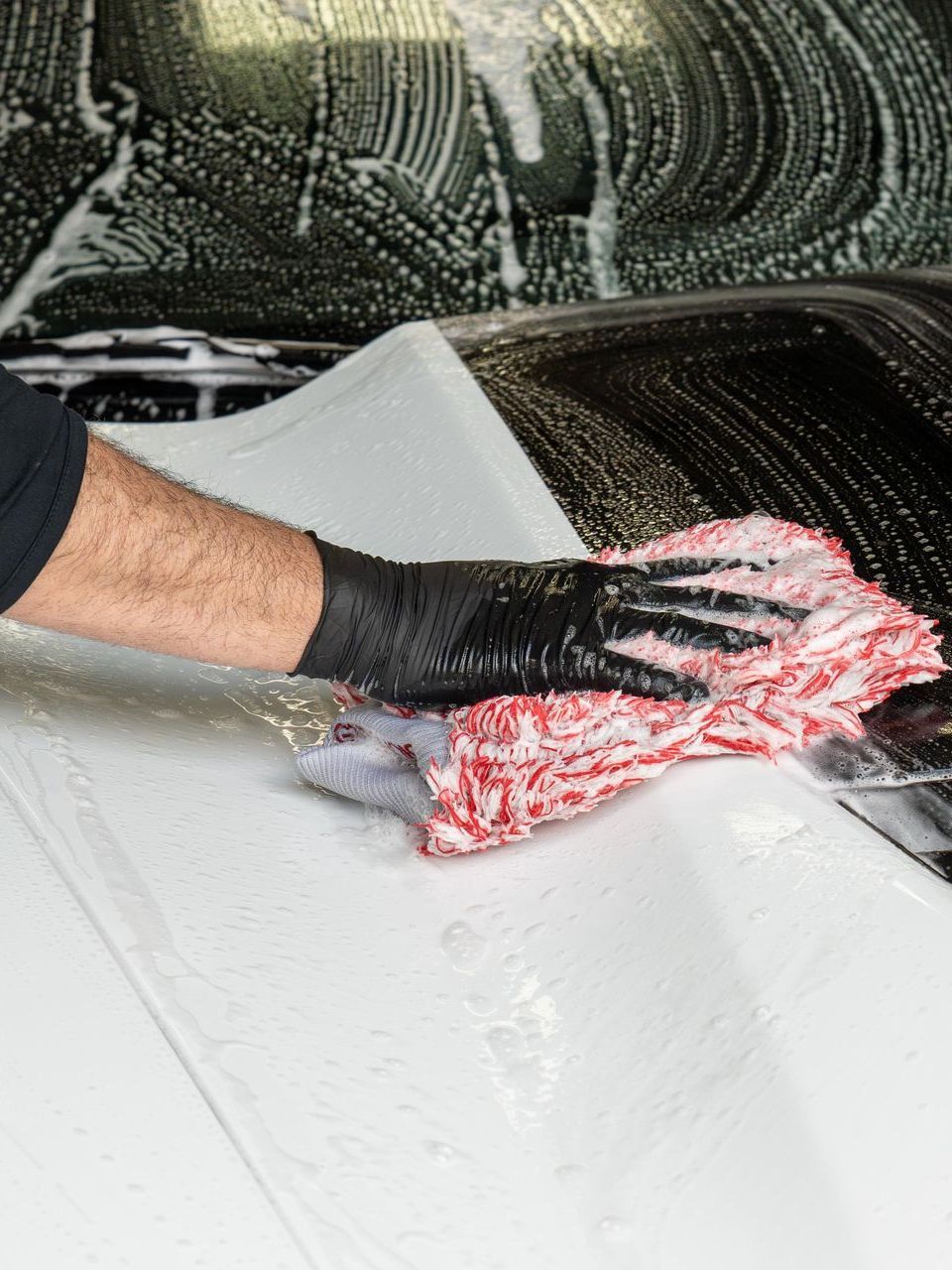 A person is washing a car with a towel and gloves.