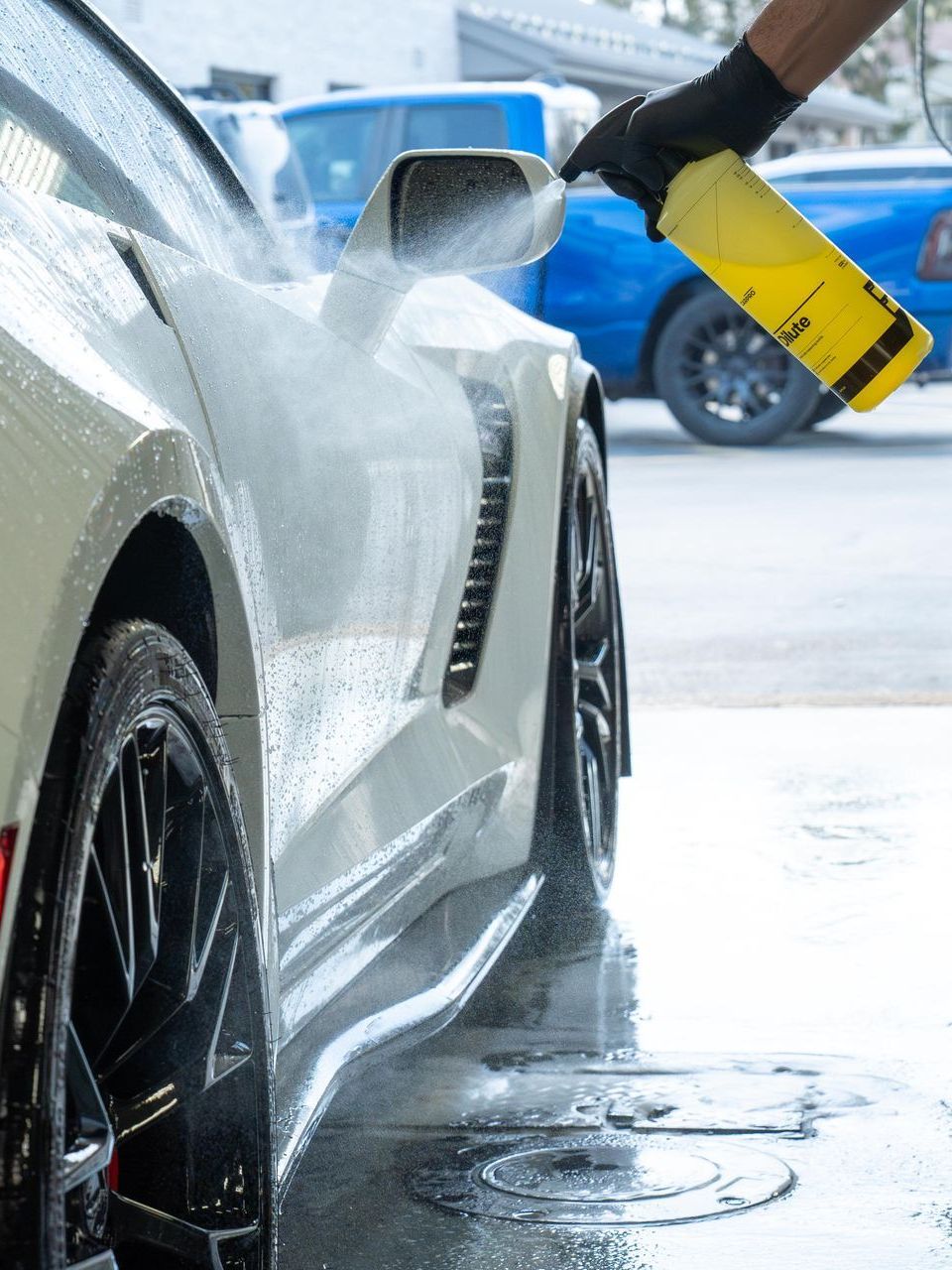 A person is washing a white car with a yellow spray bottle.
