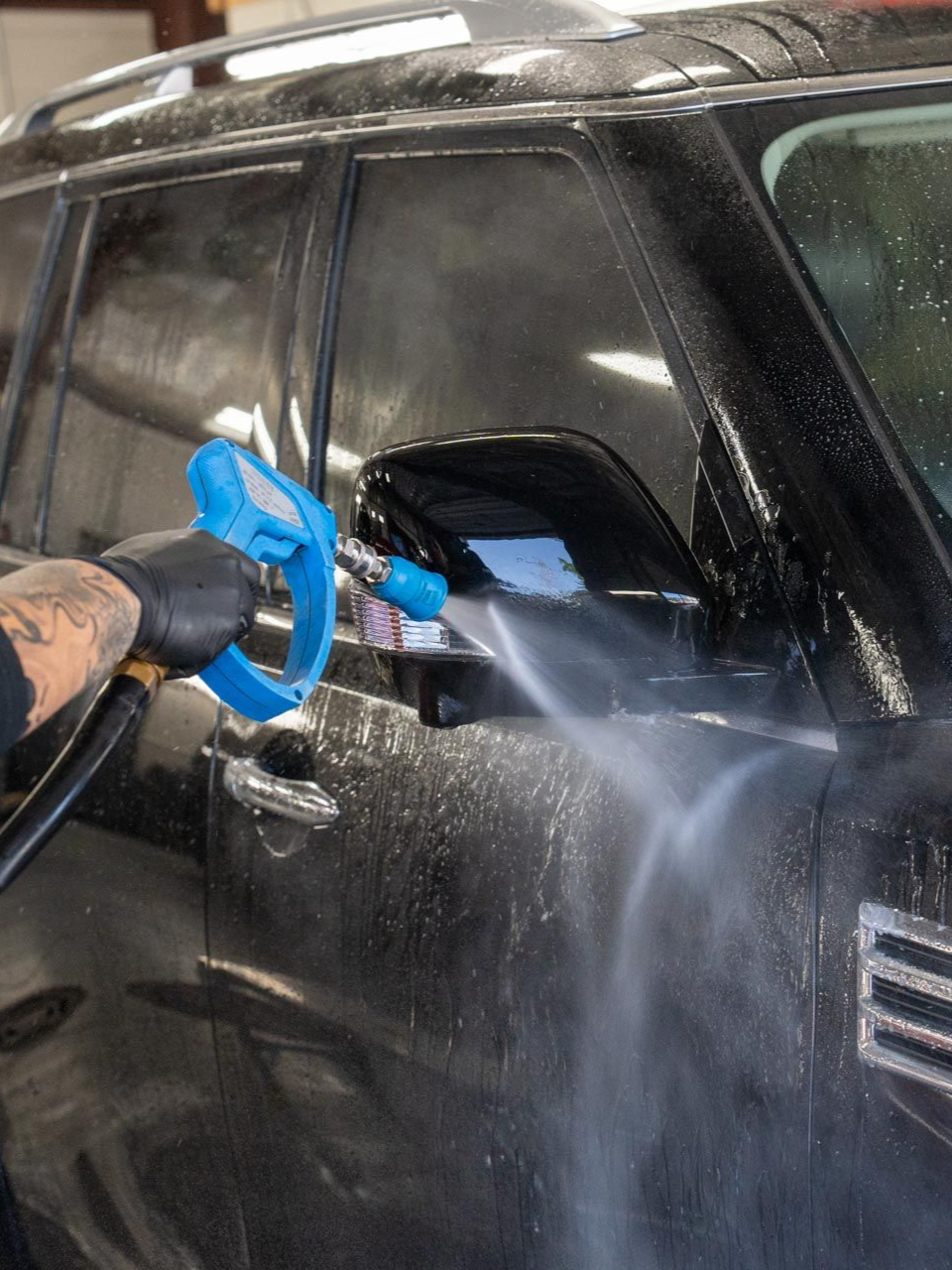 A man with a tattoo on his arm is washing a car.