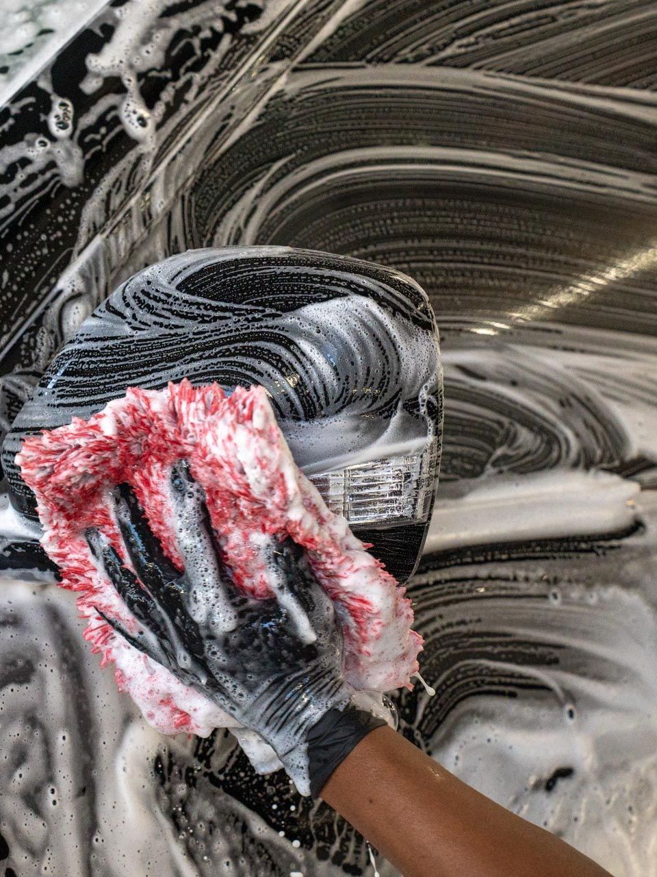 A person is washing a car with a sponge and soap.