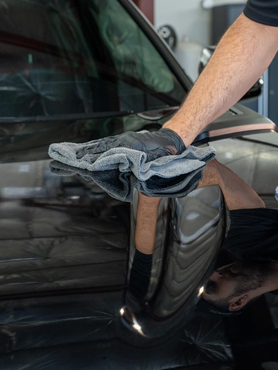 A person wearing gloves is cleaning a car with a towel.