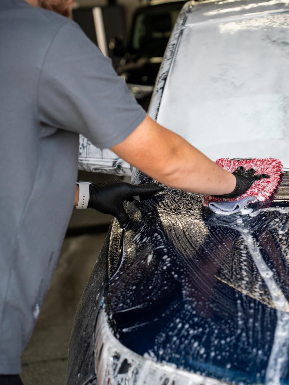 A man is cleaning the hood of a car with a cloth.