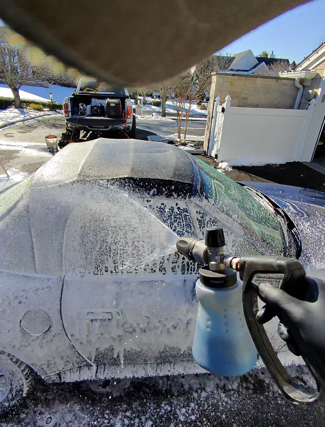 Person washing a car headlight with a soapy sponge, wearing a black glove.