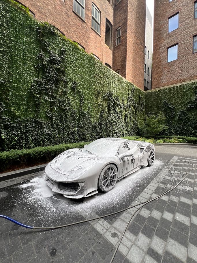car covered in foam, being washed in front of ivy-covered wall and brick buildings.