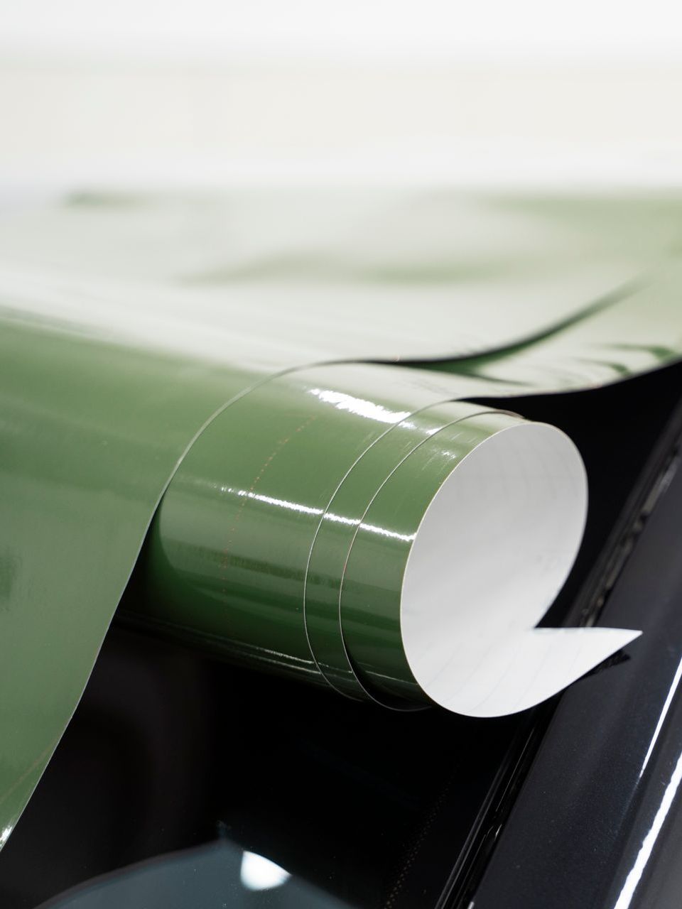 A roll of green vinyl wrap is being applied to a car window.
