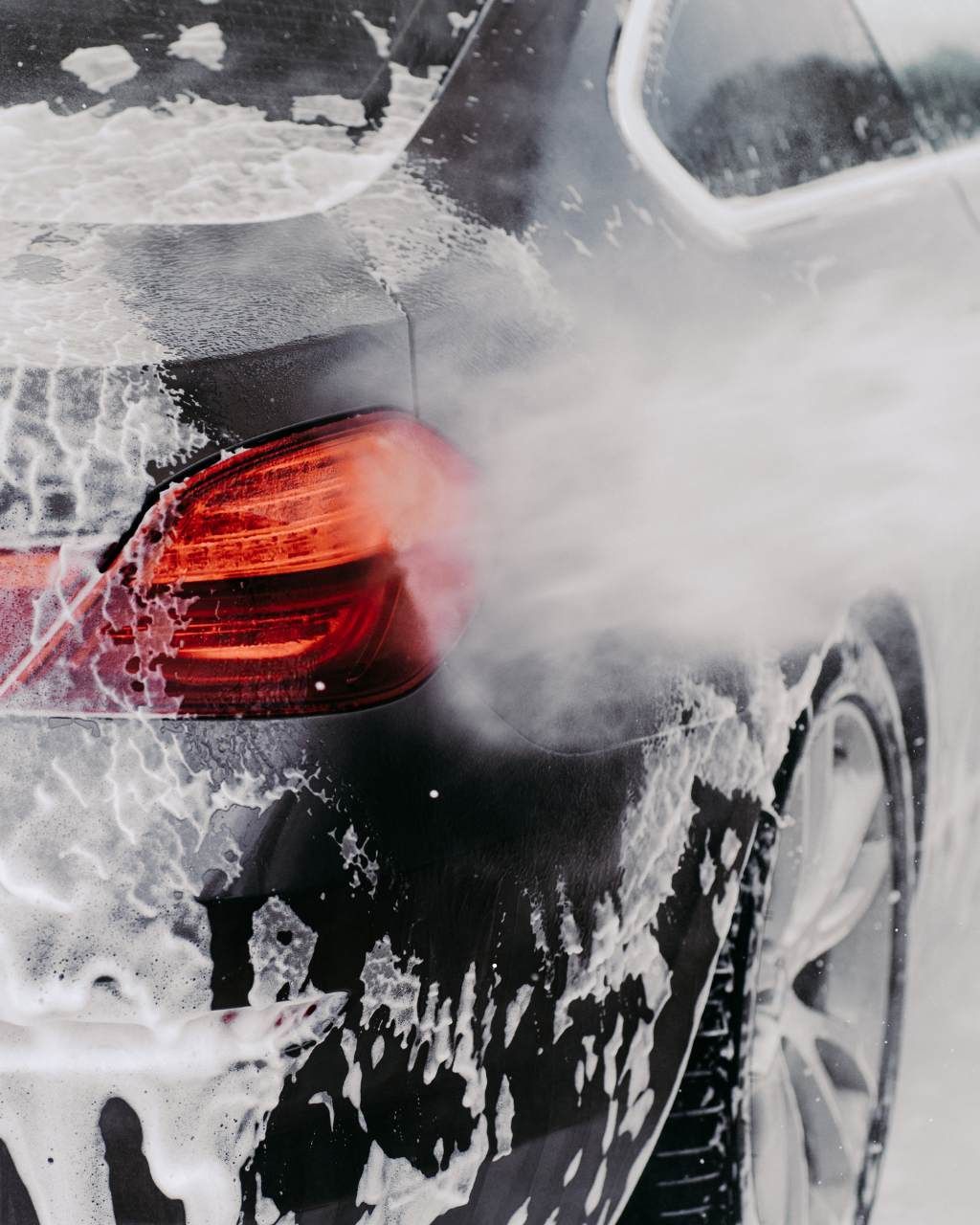 A car is being washed with a high pressure washer in a garage.