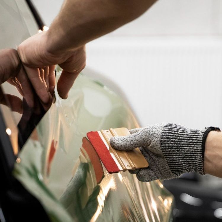 A person wearing a glove is holding a squeegee over a car window.