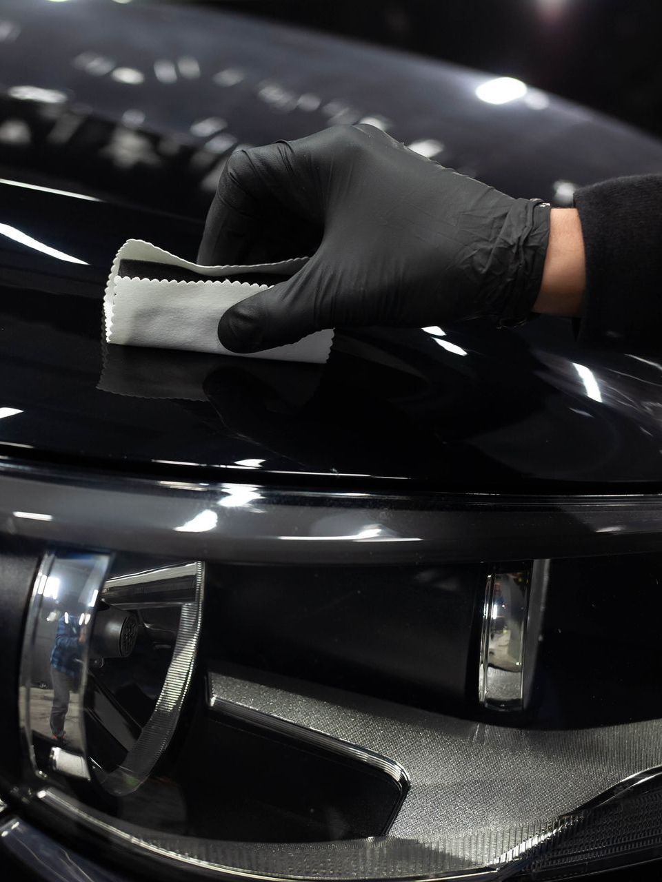 A person wearing black gloves is cleaning the hood of a car
