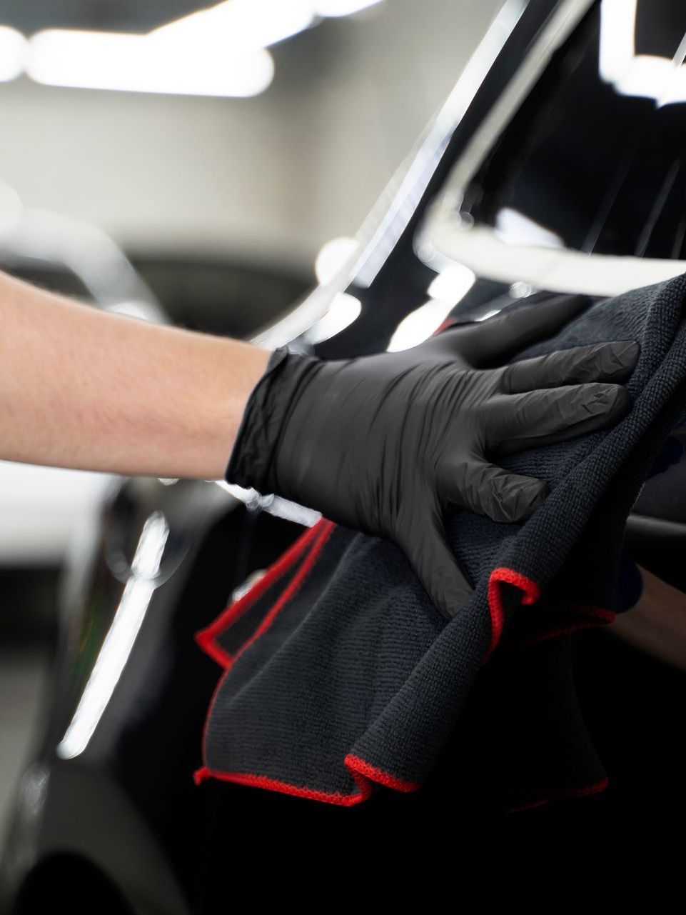 A person wearing black gloves is cleaning a car with a towel.