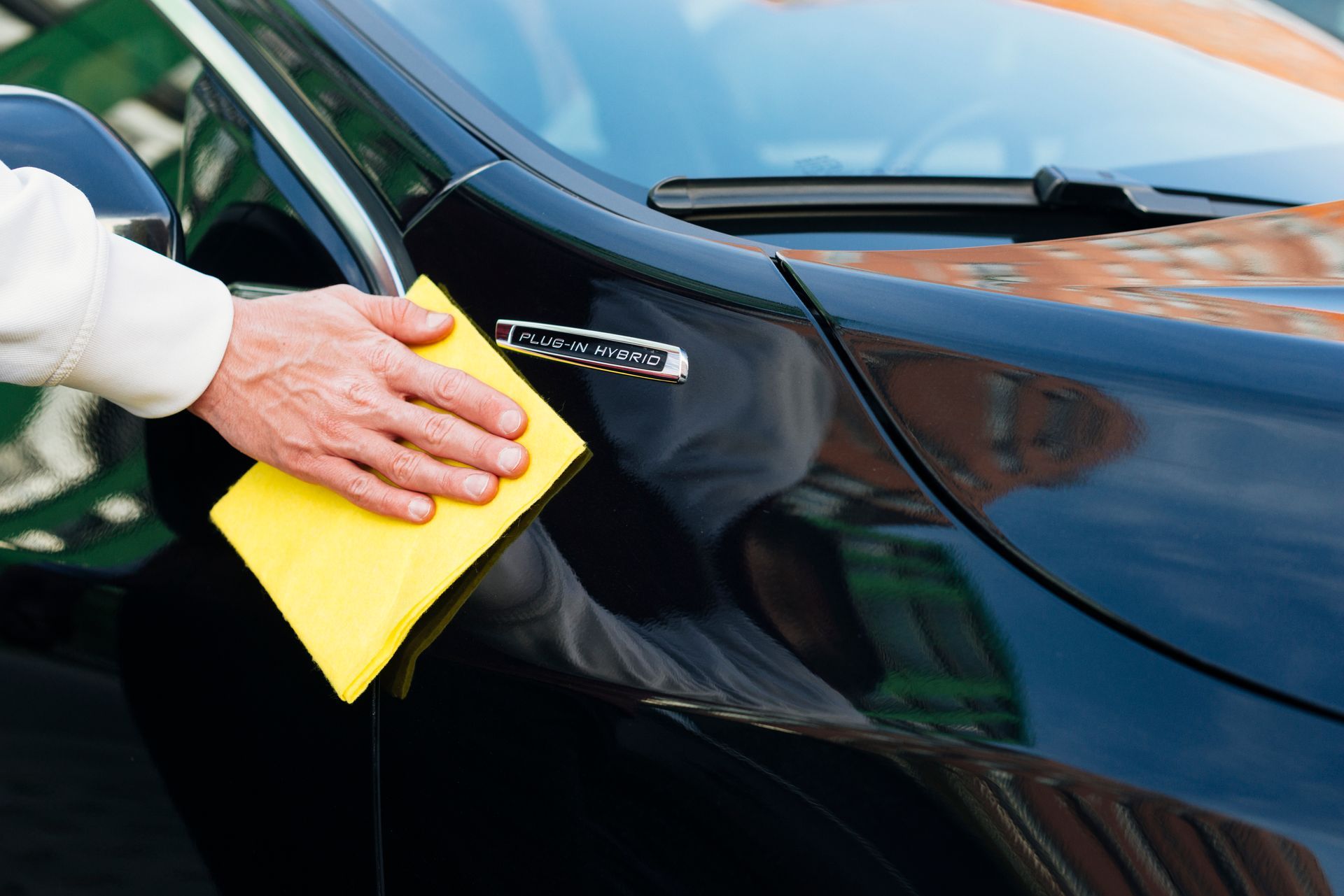 A person is cleaning a black car with a yellow cloth.