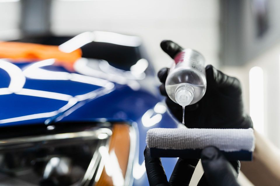 A man wearing black gloves is cleaning a black car with a blue cloth.