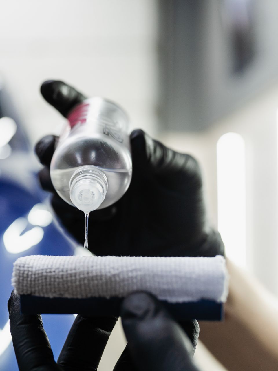 A person wearing black gloves is holding a bottle of liquid