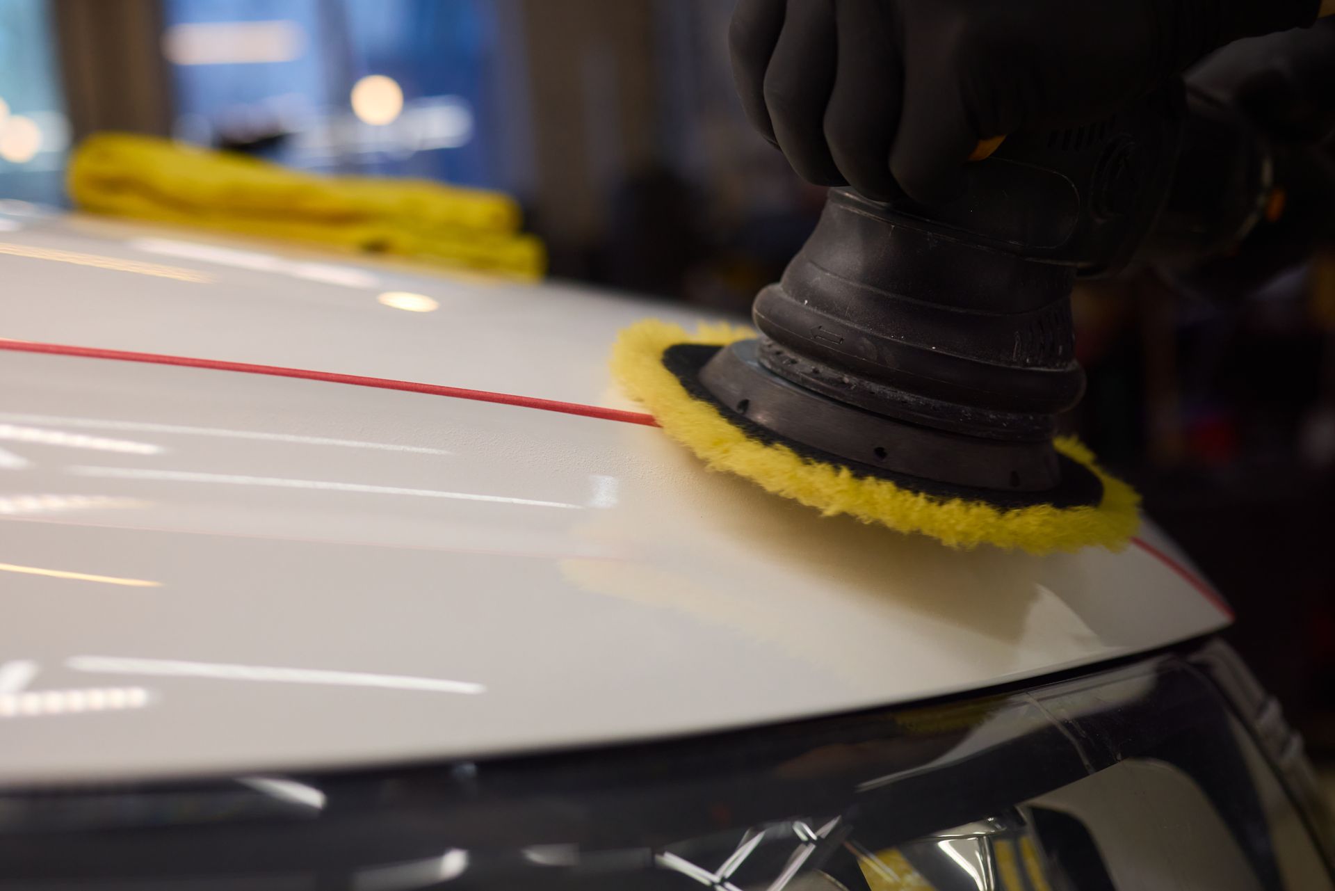 A person is polishing a white car with a yellow pad.