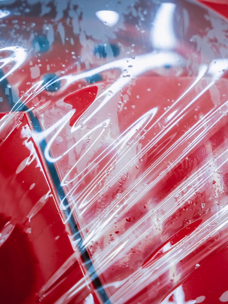 A close up of a red car covered in plastic wrap.