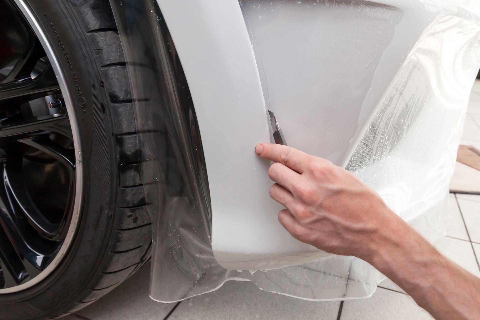 A person is applying plastic wrap to the front bumper of a car.