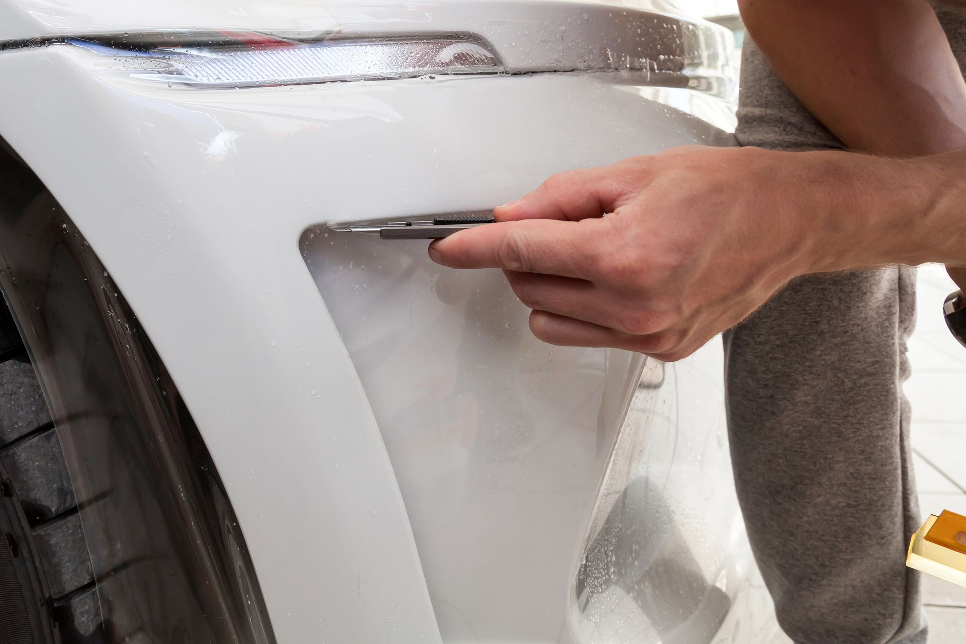 A person is applying a protective film to the fender of a white car.
