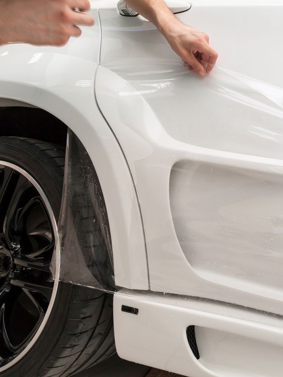 A person is applying a protective film to a white car