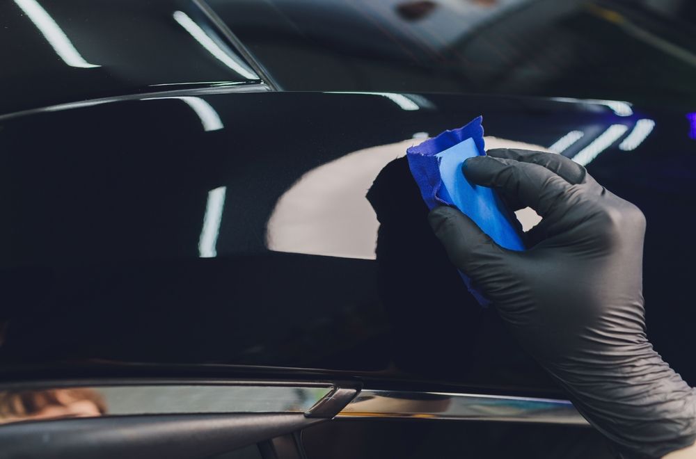 A person wearing blue gloves is cleaning the headlight of a car