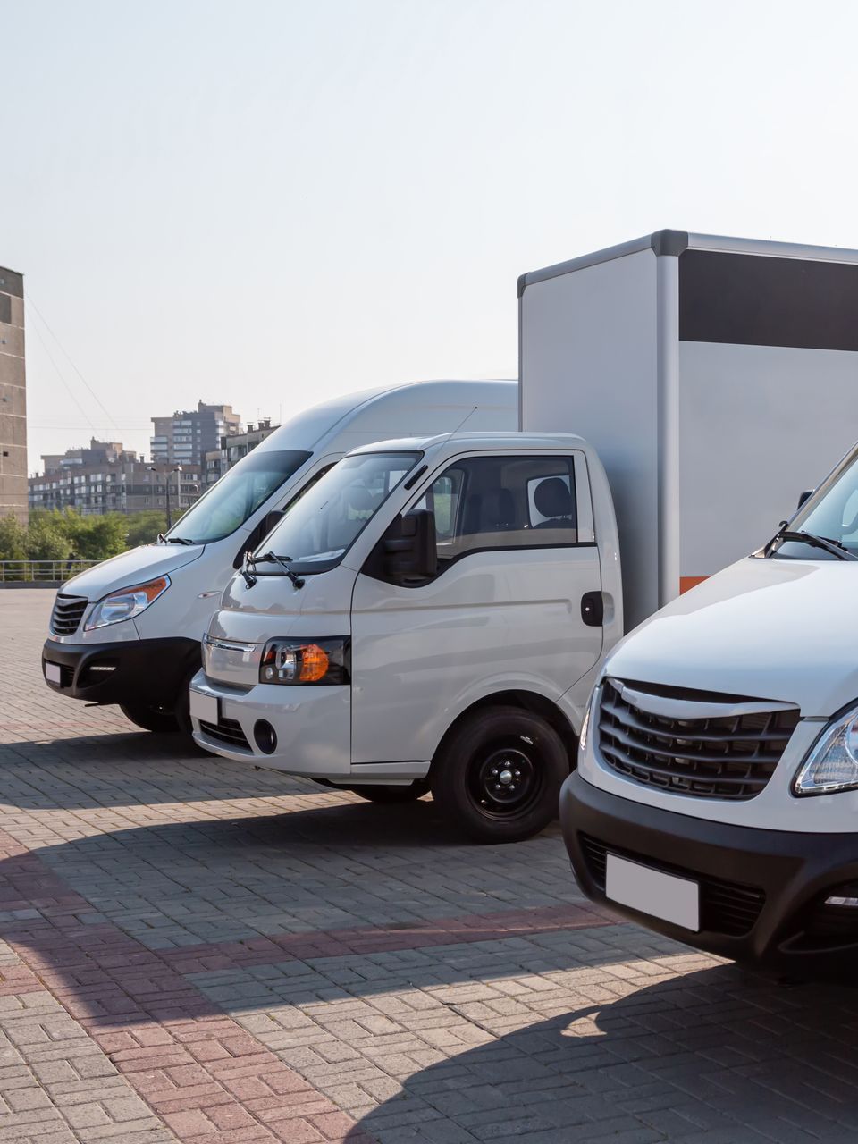 A row of white vans and trucks are parked in a parking lot.