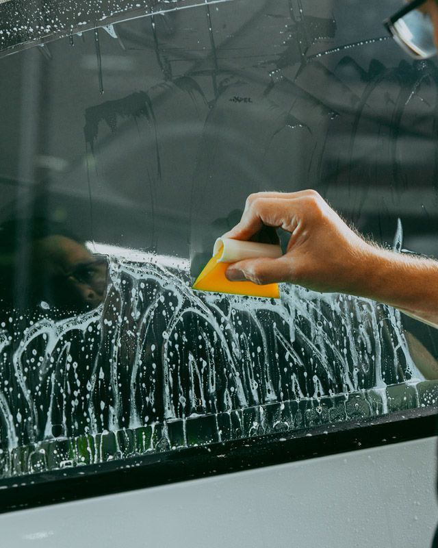 A person is cleaning a car window with a yellow sponge.