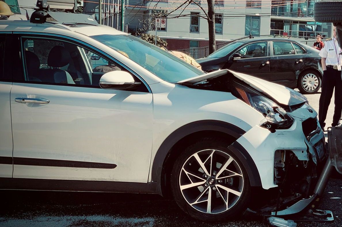 A white car with a damaged front end is parked on the side of the road.