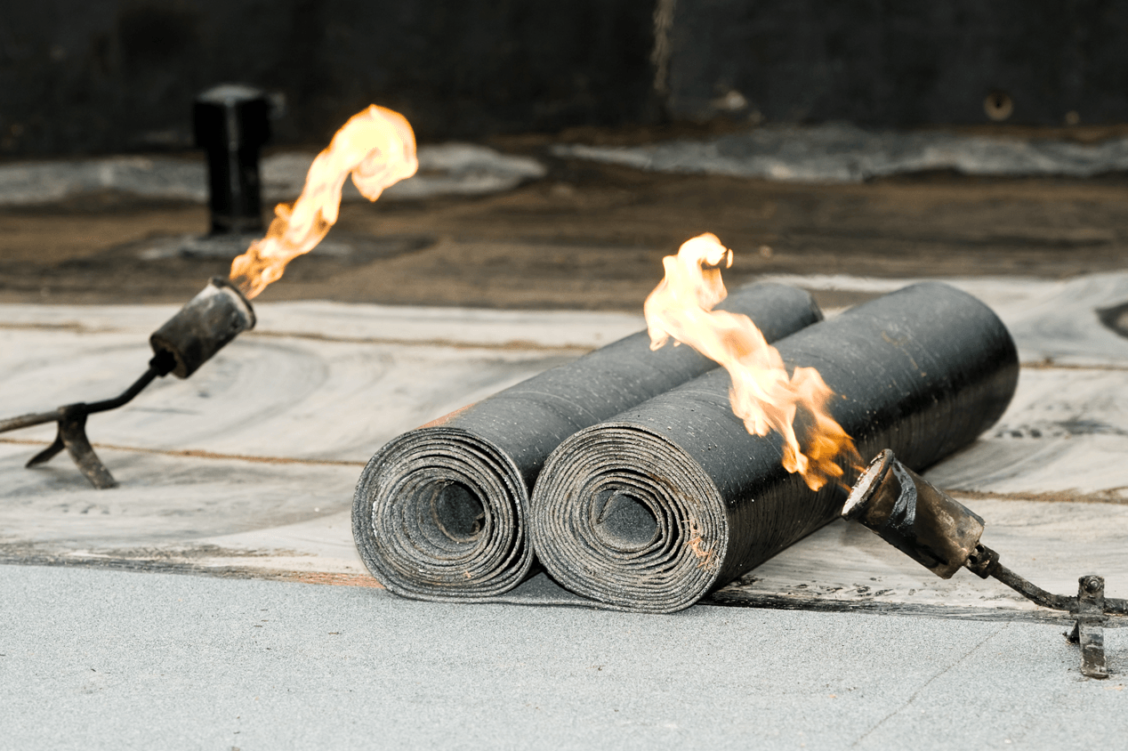 Deux bâches de toiture enroulées avec des flammes provenant de chalumeaux sur un toit.