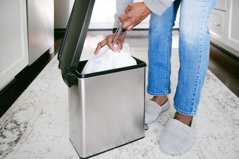 A person is putting a bag of tissues into a stainless steel trash can.