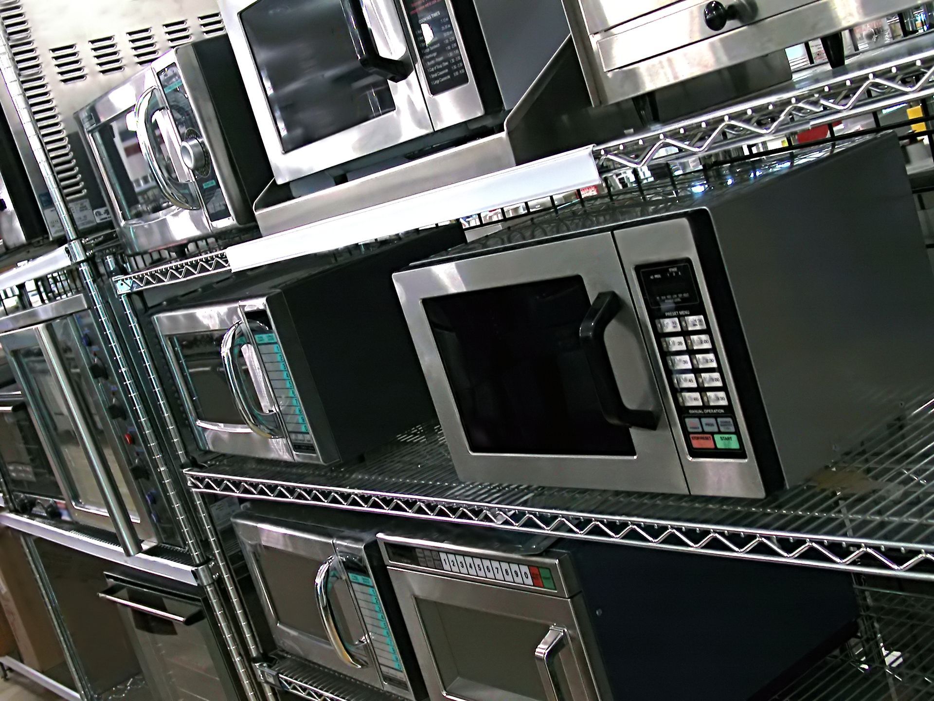 A row of microwave ovens are lined up on shelves in a kitchen.