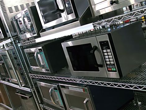 A row of microwave ovens are lined up on shelves in a kitchen.
