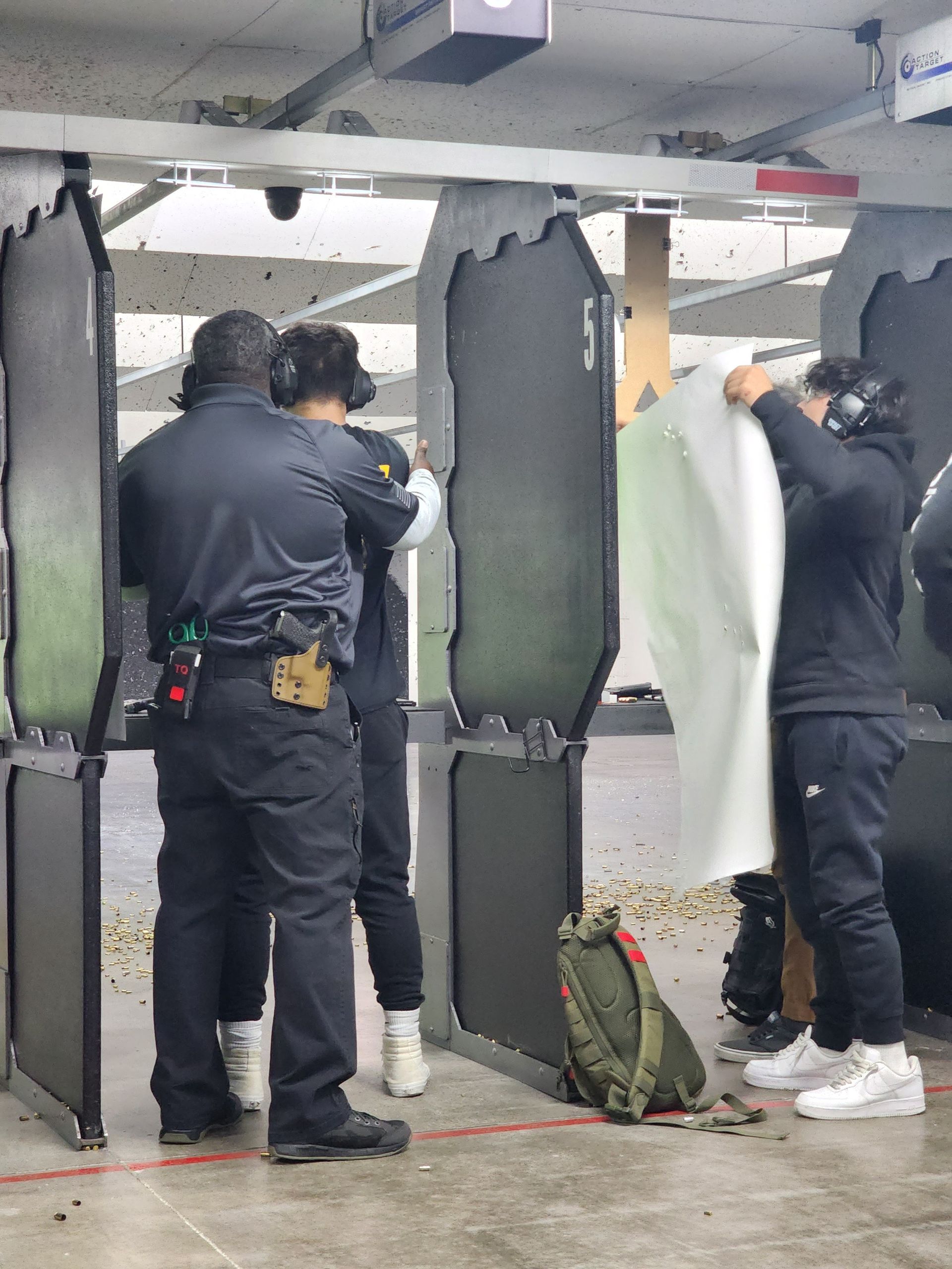 People at a shooting range: instructor, two students, targets, shooting stalls.