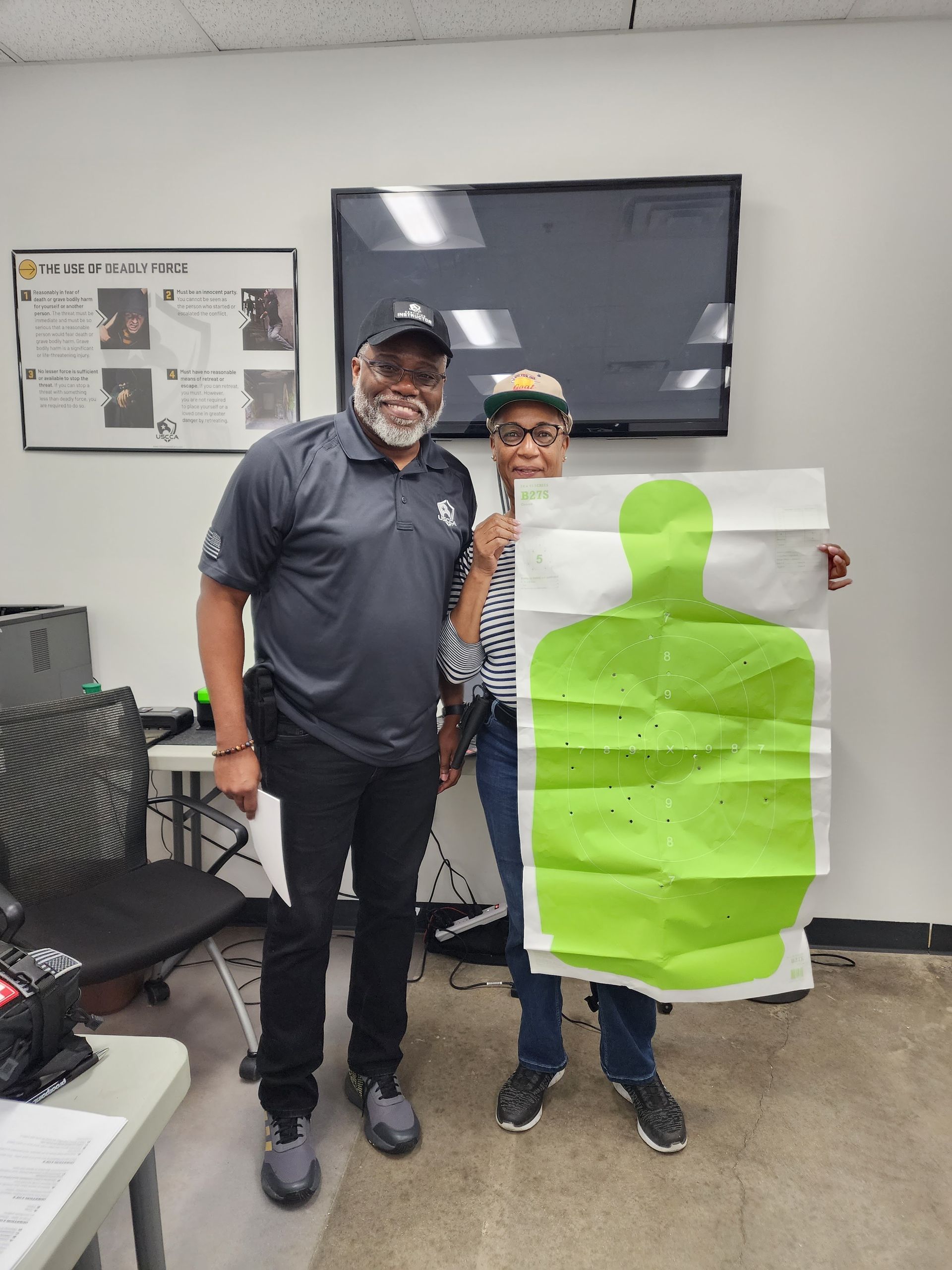 Man and woman smiling, holding target paper with bullet holes. Indoor setting.