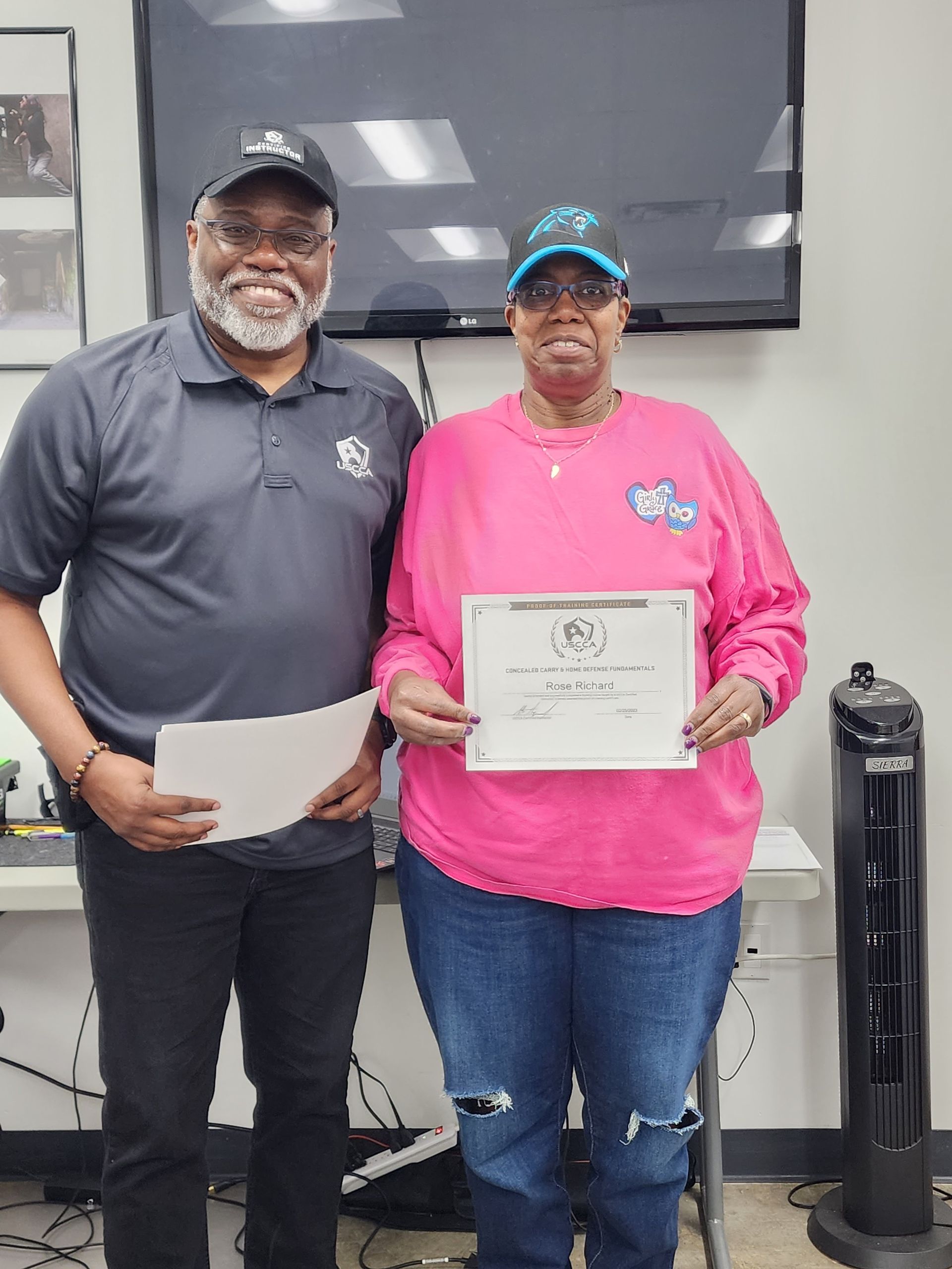 Two people, a man and a woman, pose together. The woman holds a certificate.