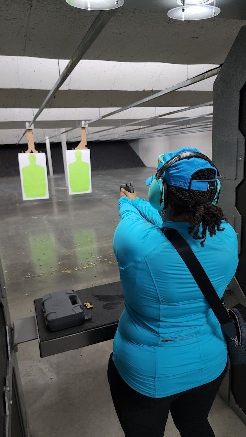 Woman in blue shooting a handgun at a target in an indoor shooting range.