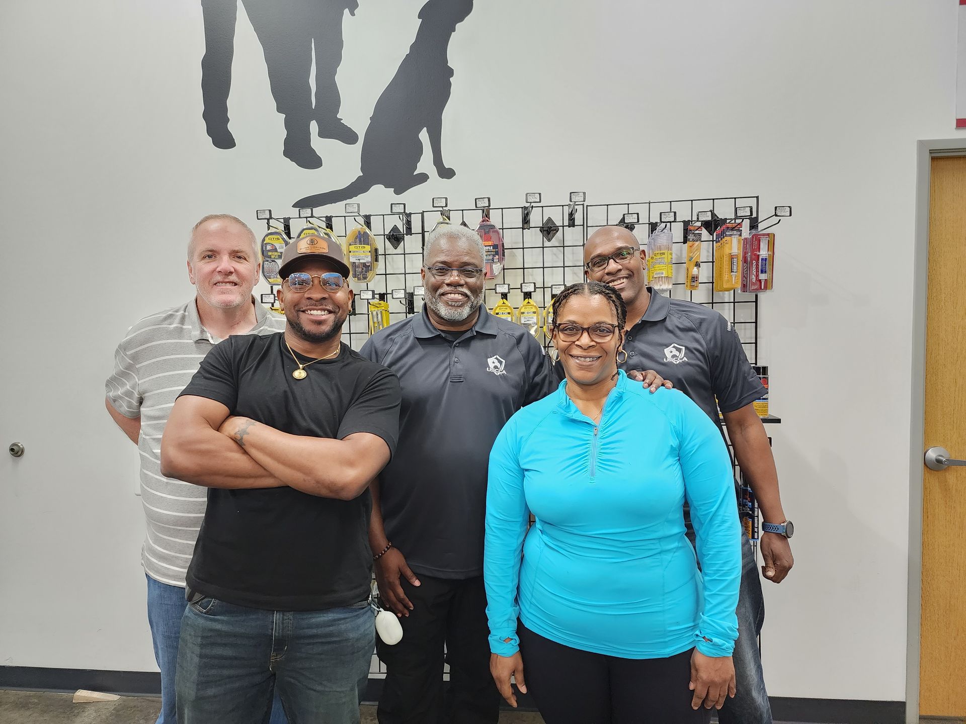 Five people smiling in a store with dog silhouettes on the wall; a woman in blue stands in front.