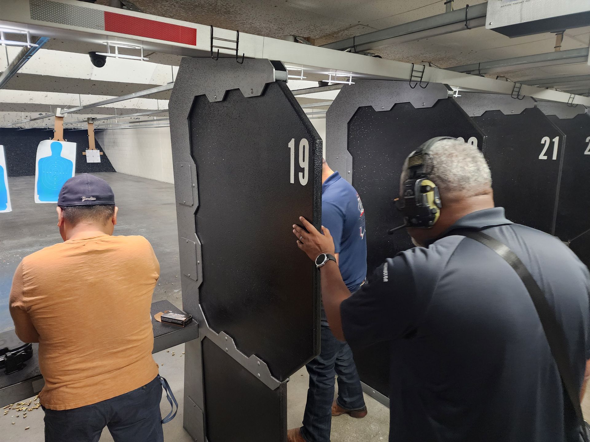 People at a shooting range, one putting up a target while others prepare to shoot.