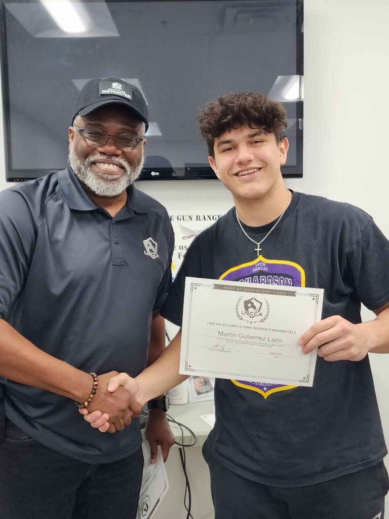 Man in hat shakes hands with a teen holding a certificate. Both smile, in a brightly lit room.