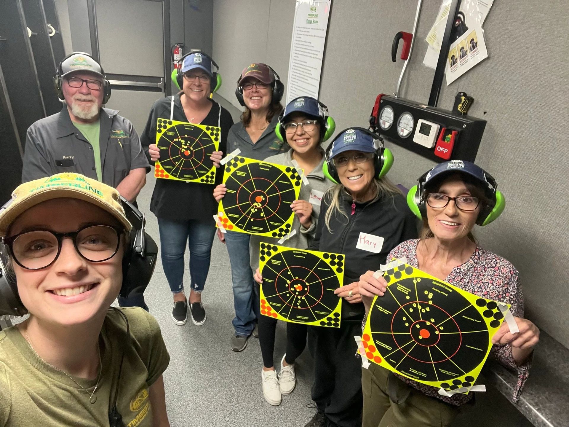 Group of people at a shooting range, smiling and holding up targets.