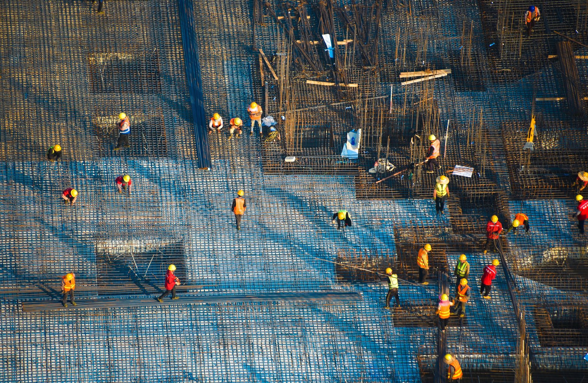 Workers prepping rebar grid at industrial site for concrete foundation construction. 
