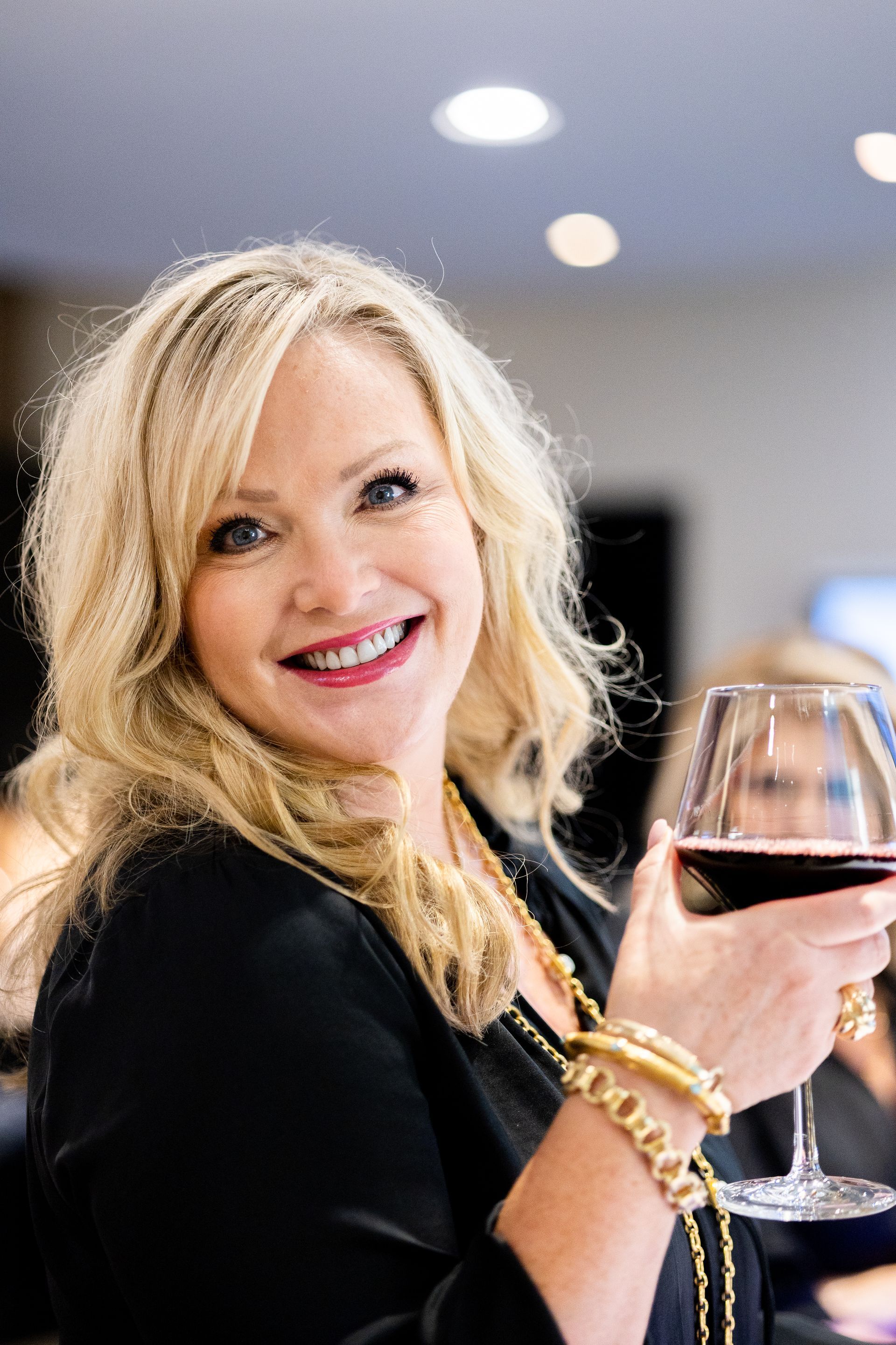 A woman is holding a glass of red wine and smiling.