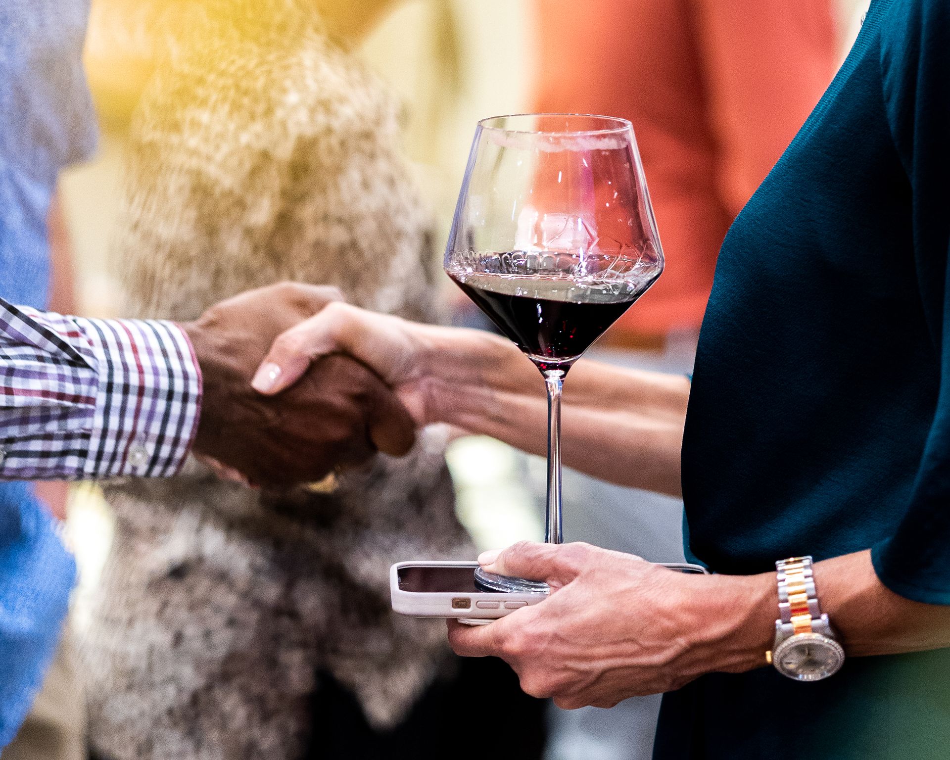 A man is shaking hands with a woman holding a glass of wine.