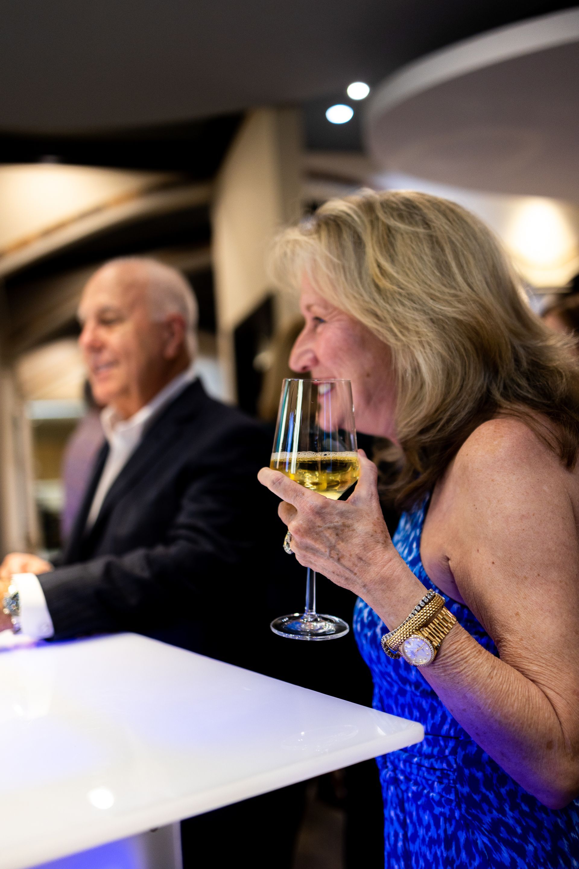 A woman in a blue dress is holding a glass of wine