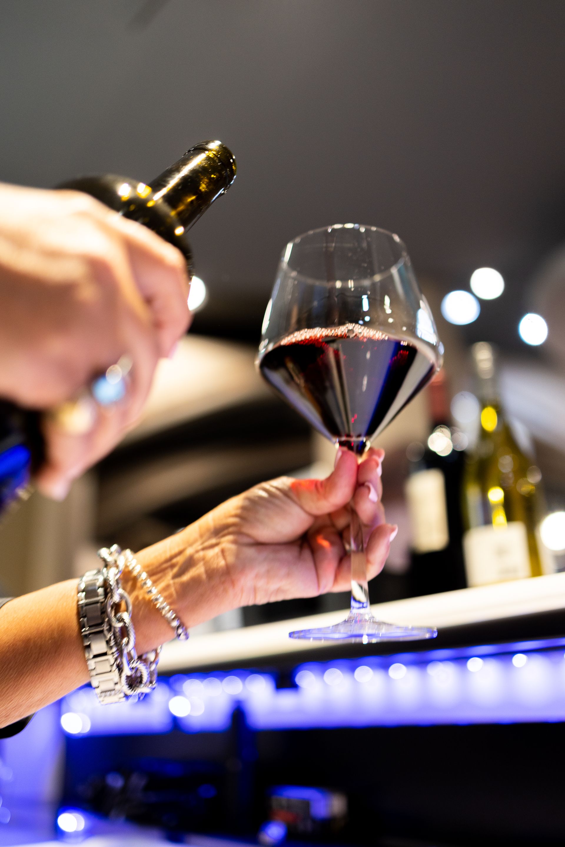 A woman is pouring a glass of red wine from a bottle.