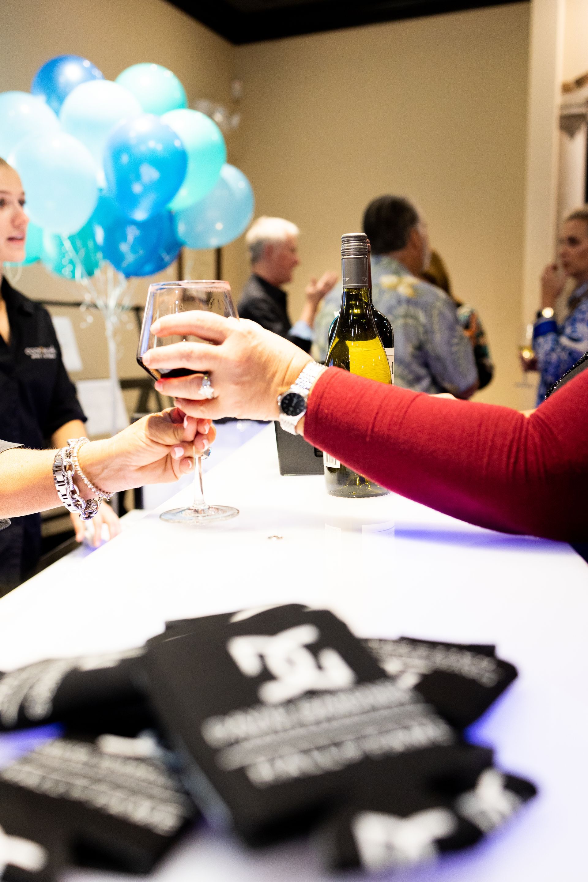 A woman is holding a glass of wine at a table with balloons in the background.