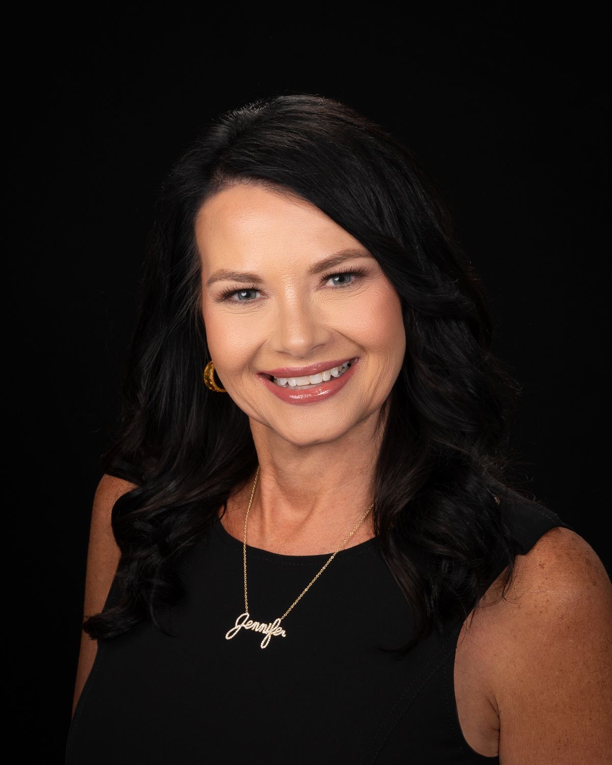 A woman in a black dress and necklace is smiling for the camera.