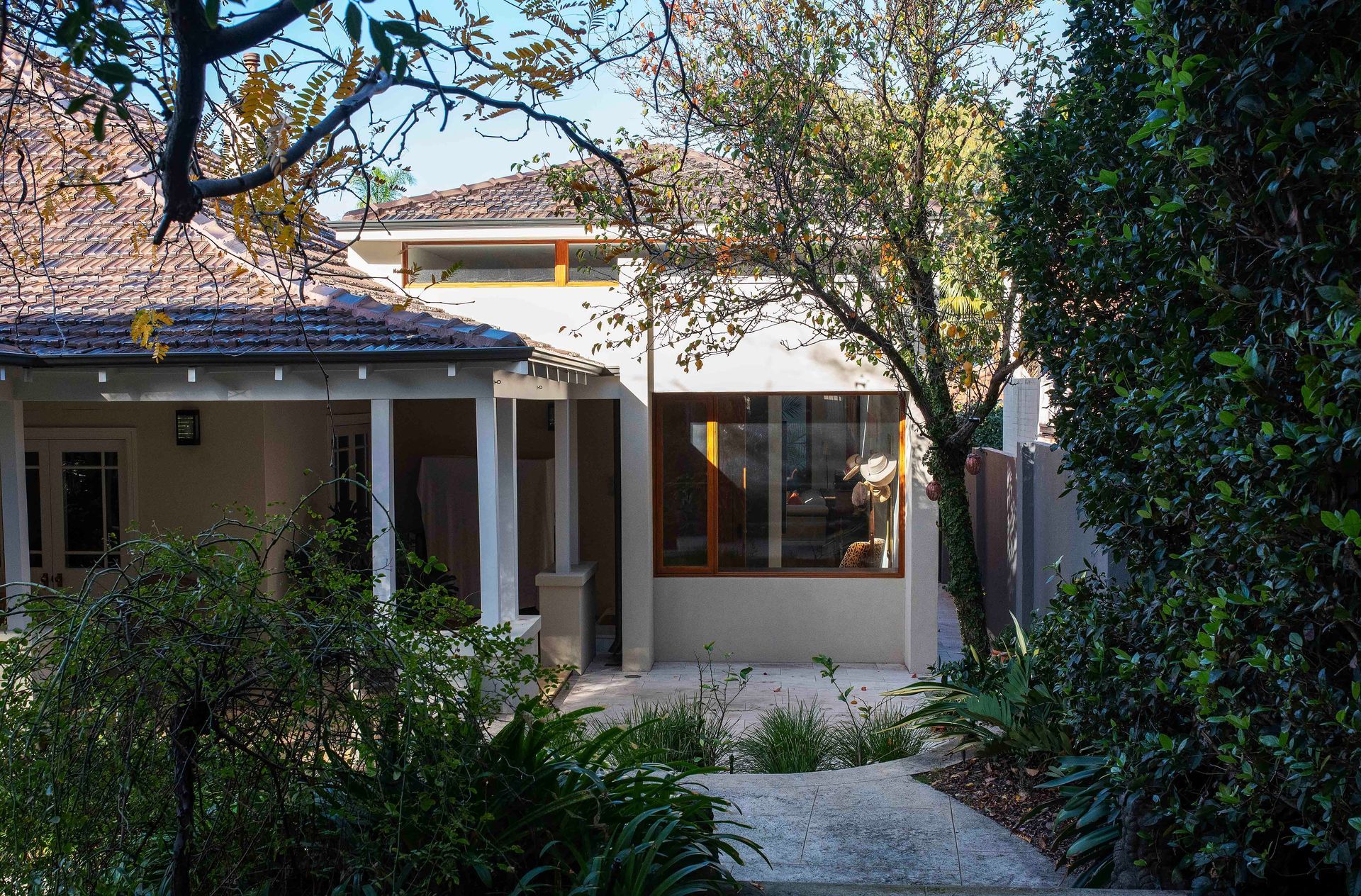 Exterior view of a modern cottage with a shingled roof, surrounded by lush green foliage and trees