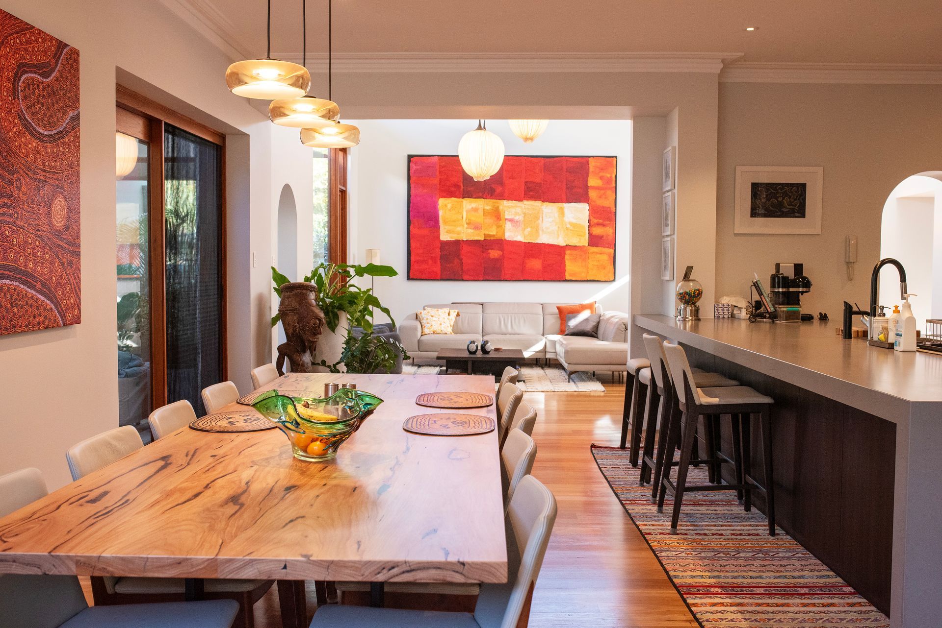 Modern open-plan kitchen and dining area featuring a long wooden dining table, contemporary lighting, and warm interior décor